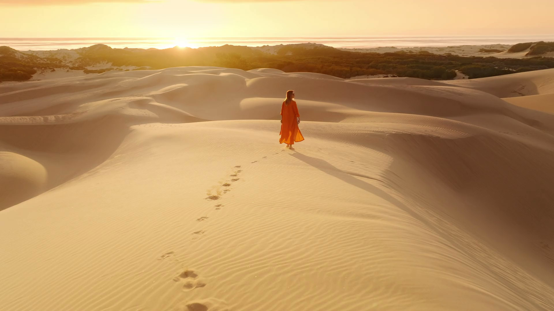 A woman in light desert clothing walking in the dunes